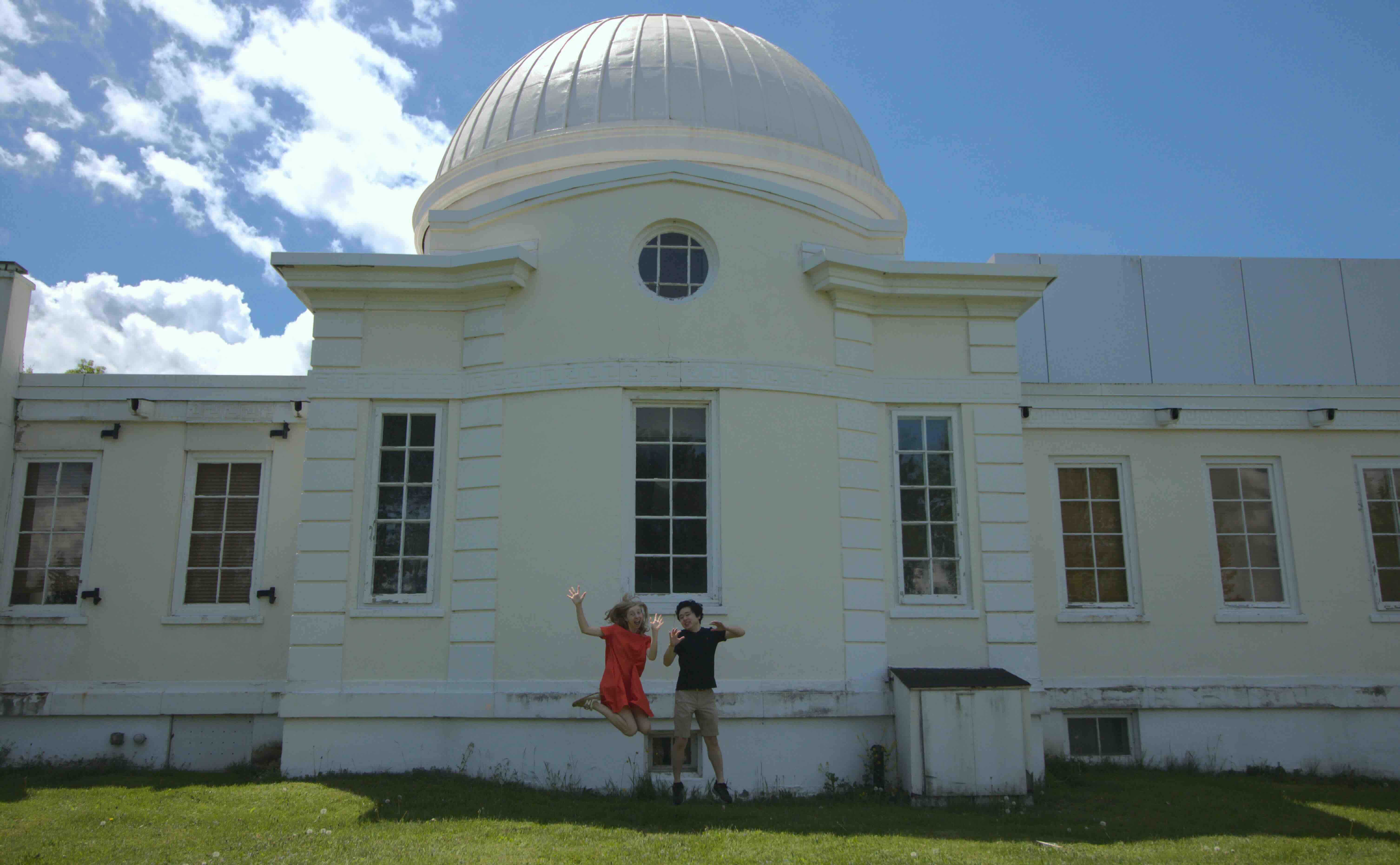 Two people jumping behind the Fuertes Observatory