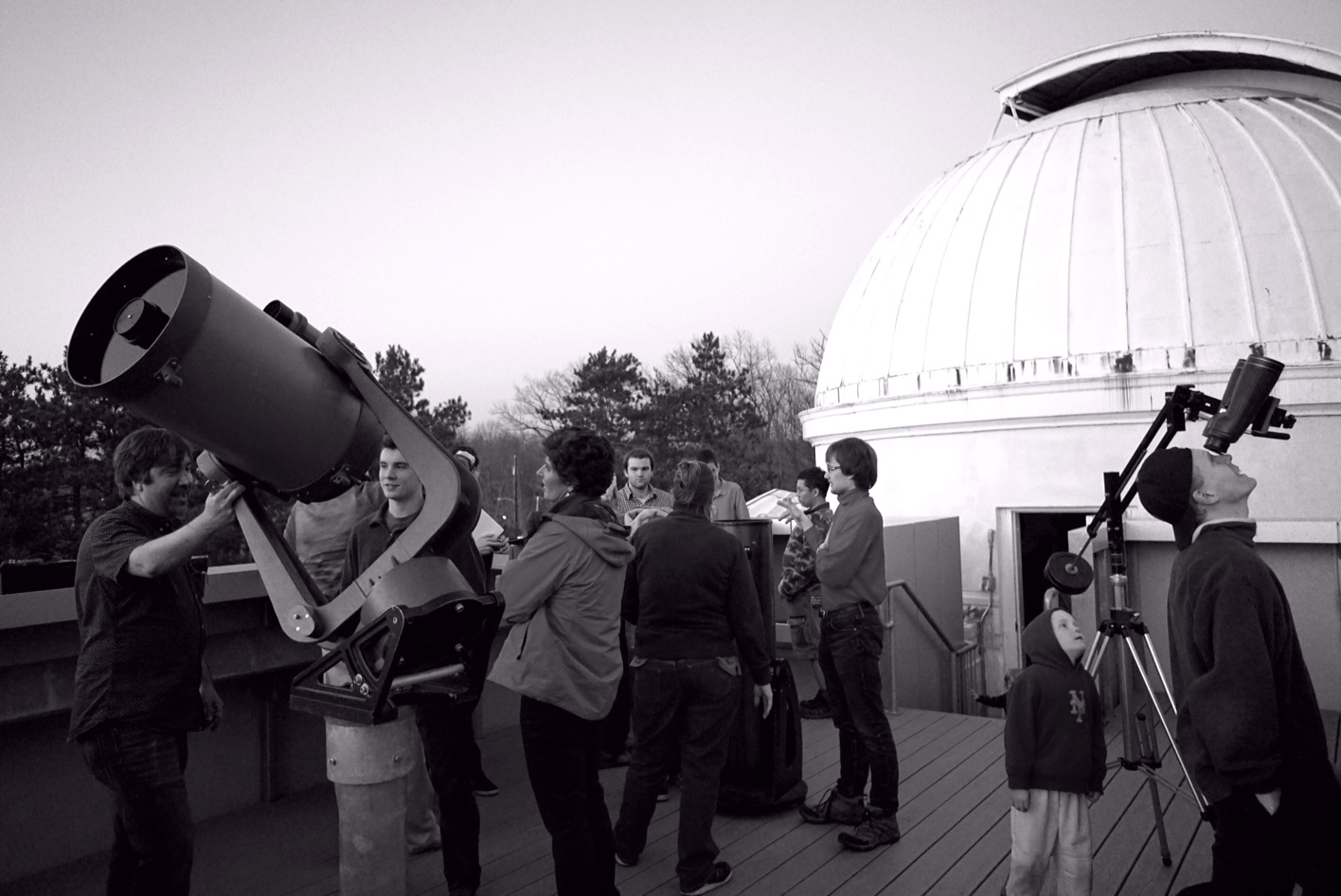 Observing deck during an open house night. Members and visitors are seen using a Celestron 14-inch Schmidt-Cassegrain telescope, an Orion 10-inch Dobsonian telescope, and a pair of binoculars.